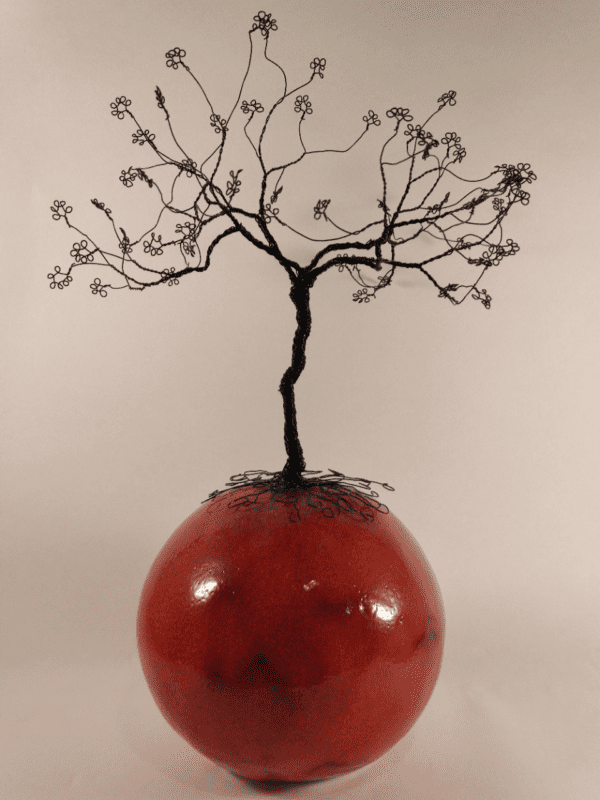 arbre de vie en fil de fer noir posé sur une boule en céramique émaillée rouge feu. Vue de près sur la boule