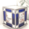 Lampe vitrail Azulero en forme de cube. Dessins d'oiseaux sur les quatre faces et bordure en verre bleu et miroir. Lampe présentée de trois quart éteinte