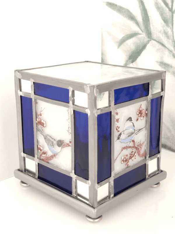Lampe vitrail Azulero en forme de cube. Dessins d'oiseaux sur les quatre faces et bordure en verre bleu et miroir. Lampe présentée de trois quart éteinte