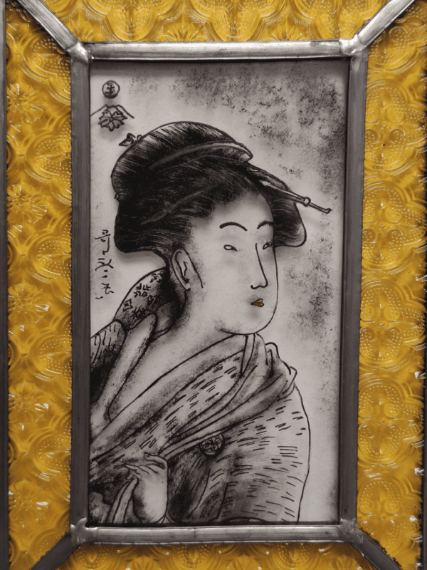 Petit médaillon Baldine. Il représente un portrait de Geisha peint à la grisaille noire. Il a un liseré en verre jaune avec des impression