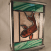 Lampe vitrail Carpe Koï. Une carpe Koï orange est dessinée au centre de la lampe. les bords de lampe sont dans du verre marbré vert et transparent. Lampe vue de trois quart