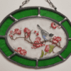 médaillon Cestya de forme ovale avec chainette d'accroche et un liseré vert. Il représente un petit oiseau sur une branche de cerisier