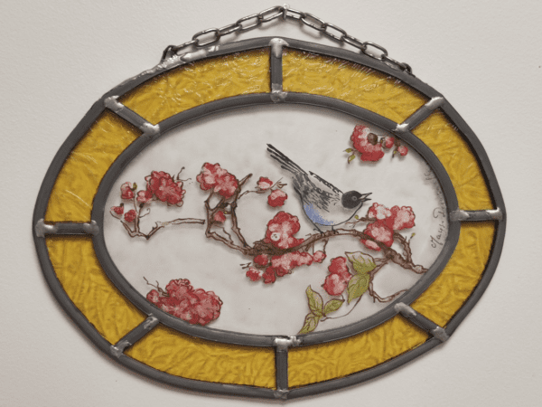 Médaillon Floria avec une chainette d'accroche, en forme de losange avec un liseré jaune. Il représente un oiseau sur une branche de fleur de cerisier