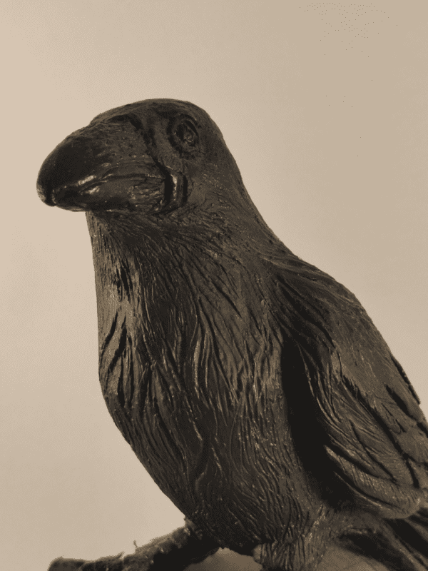 Corbeau en céramique patinée noire et or posé sur un tronc d'arbre, vu de trois quart face