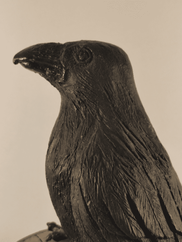 Corbeau en céramique patinée noire et or posé sur un tronc d'arbre, vu de profil