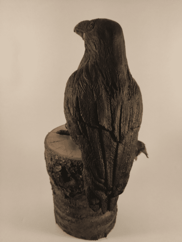 Corbeau en céramique patinée noire et or posé sur un tronc d'arbre, vu de dos