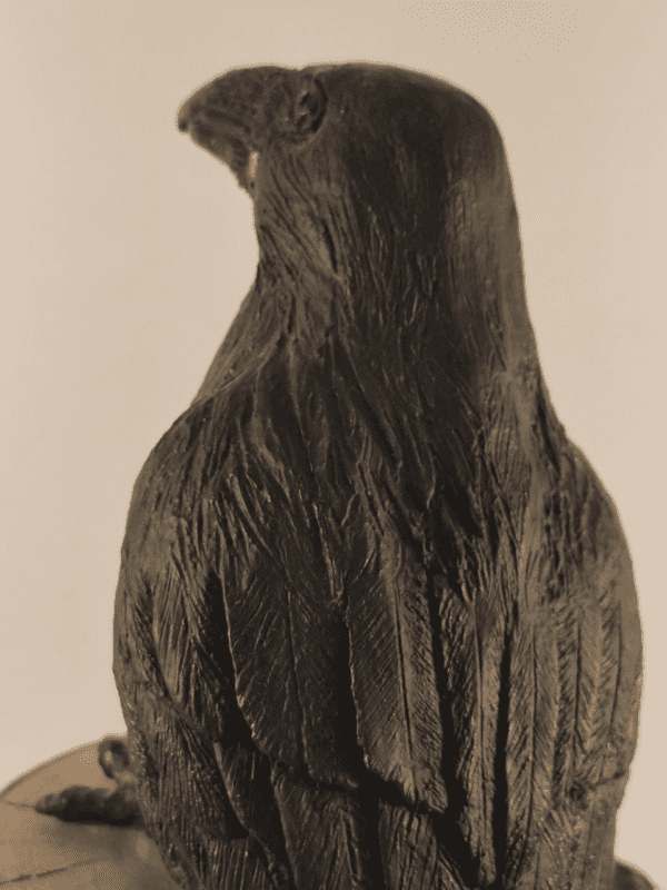 Corbeau en céramique patinée noire et or posé sur un tronc d'arbre, vu de dos