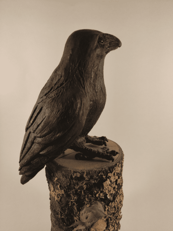 Corbeau en céramique patinée noire et or posé sur un tronc d'arbre, vu de profil