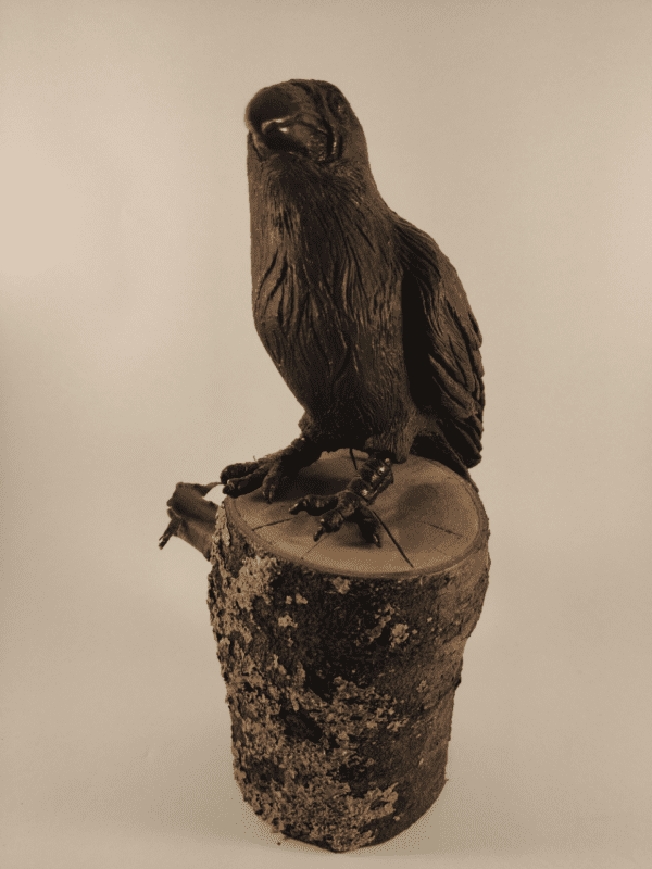 Corbeau en céramique patinée noire et or posé sur un tronc d'arbre.