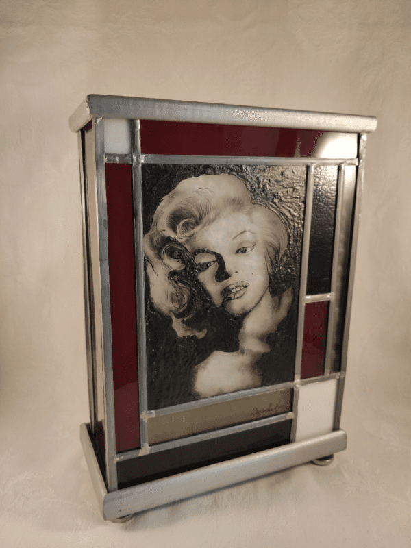 Lampe vitrail Marilyne. Portrait de Marilyne Monroe avec des bords rouges et noirs vue de trois quart. Lampe éteinte