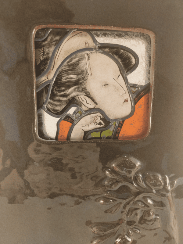 Vitrail représentant le portrait d'une geisha. Il est inséré dans un cadre en céramique émaillé vert avec des roses en relief. Vue de près. Elle s'intitule Mouna