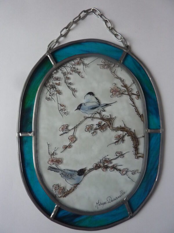 médaillon ovale avec une chainette permettant de l'accrocher. Il à un liseré bleu et son centre est décoré avec trois mésanges sur des branches de cerisiers en fleur. Il s'intitule Pitouine