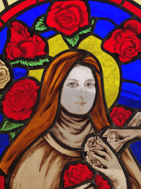 vitrail de Sainte Thérèse de Lisieux entouré de roses. Vue du portrait avec la main qui tient un crucifix avec le Christ