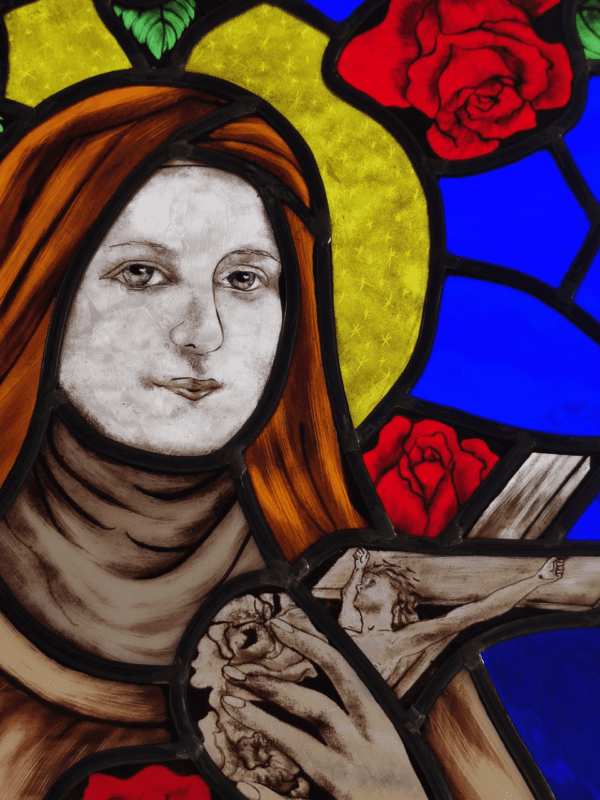 vitrail de Sainte Thérèse de Lisieux entouré de roses. Vue du portrait avec la main qui tient un crucifix avec le Christ