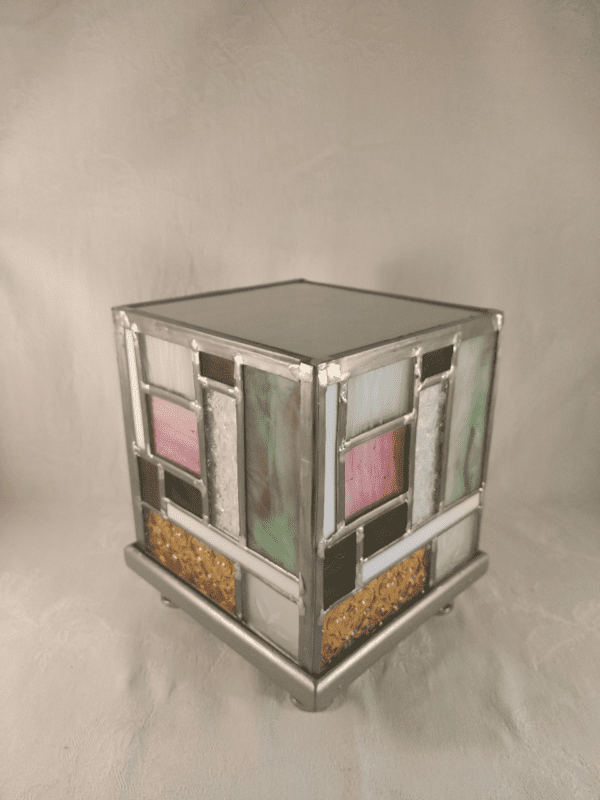 lampe en vitrail éteinte en forme de cube d'inspiration Mondrian en jaune, vert et rose. elle est présentée de trois quart. Elle s'intitule Tyni