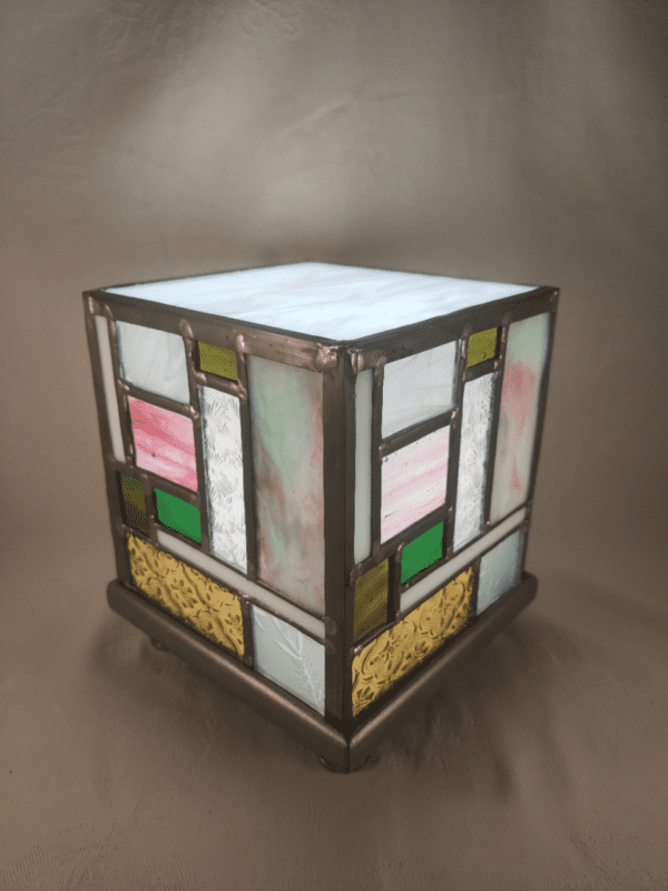 lampe Tiny en vitrail allumée en forme de cube d'inspiration Mondrian en jaune, vert et rose. elle est présentée de trois quart. Elle
