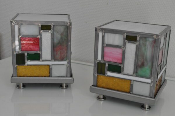 deux lampes Tyni éteintes en vitrail. Elles sont en forme de cube d'inspiration Mondrian en rose, jaune et vert. Ces lampes peuvent servir de lampe de chevet